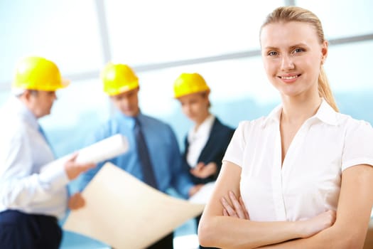 Portrait of beautiful architect folding arms on the background of workers