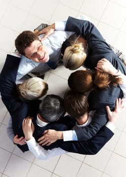 Above view of several business partners embracing each other while making circle with one of them looking at camera