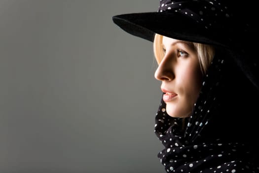 Profile of elegant young woman wearing black hat with polka dot scarf over it