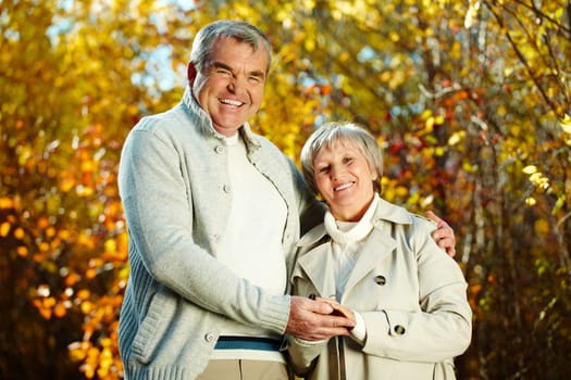 Photo of happy aged man and woman looking at camera in autumnal park