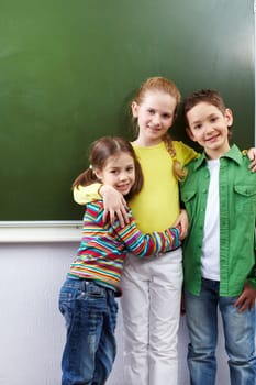 Group of happy classmates looking at camera by whiteboard