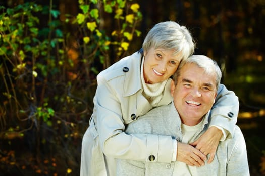 Photo of amorous aged man and woman looking at camera in autumnal park