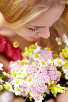 Portrait of young woman holding bunch of chamomiles and smelling it