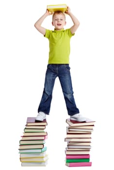 A cheerful boy with a book standing on two heaps of books