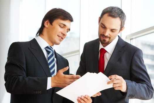 Image of confident businessman looking at document in partners hand while discussing it