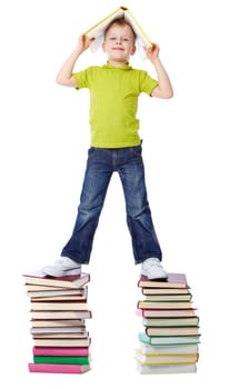 A cheerful boy standing on two heaps of books and holding a book over his head