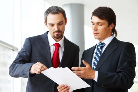 Image of confident businessman looking at document in partners hand while discussing it
