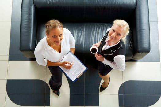 Above angle of two friendly employees standing by sofa and looking at camera