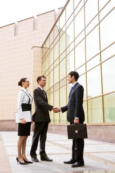 Portrait of two businessmen shaking hands after signing contract with pretty employee standing near by