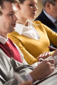 Confident businessman writing summary of his work with woman at background
