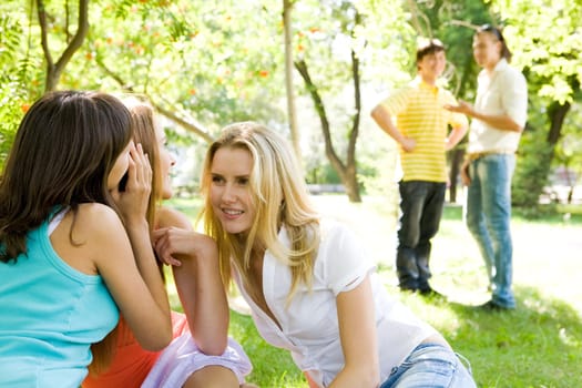 Photo of three girls whispering around each other and looking at guys on background