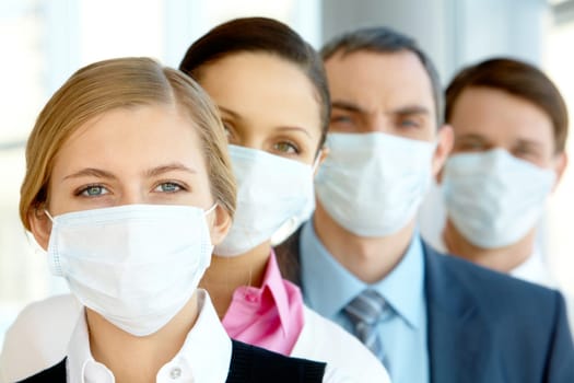Pretty female in protective mask looking at camera with row of partners behind