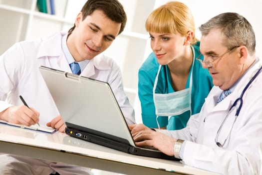 Three specialists looking at laptop screen while elderly man typing document