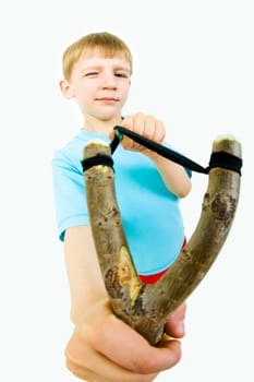 Photo of young boy holding slingshot in front of himself and looking at camera with one eye closed