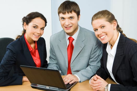 Group of three business people sitting at the table and looking at camera