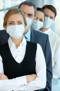 Pretty female in protective mask looking at camera with row of partners behind
