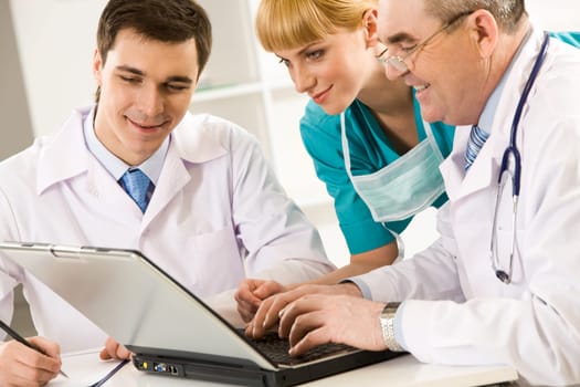 Three therapists looking at laptop screen while elderly man pressing keypad buttons