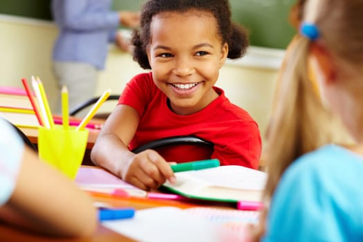 Portrait of cute girl giving crayon to classmate at lesson