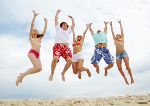 Photo of five friends in high jump over sandy beach