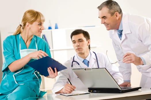Photo of aged physician and young clinician looking at document in nurses hand