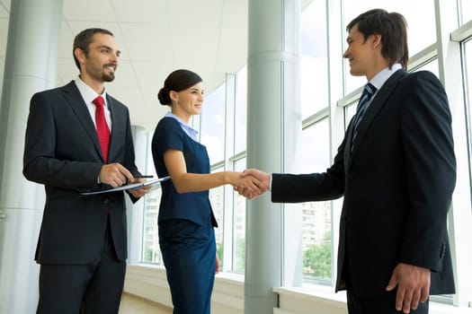 Photo of successful business partners handshaking after striking great deal with smiling man near by