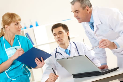 Photo of aged physician and young clinician looking at document in nurses hand