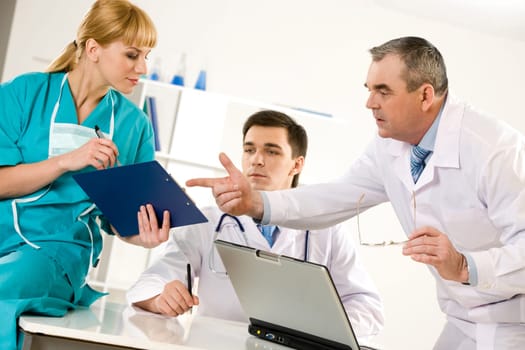 Photo of aged physician pointing at document in nurses hand with their colleague beteen them