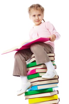 A little girl with a book sitting on a heap of books