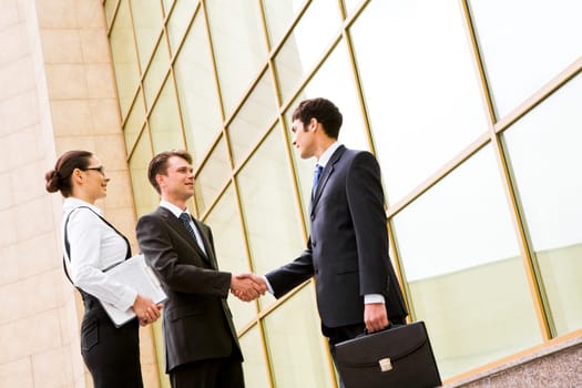 Portrait of successful partners handshaking after making agreement with elegant secretary near by