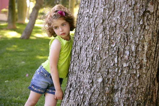 Beautiful blue eyes little girl and a tree on the park green grass