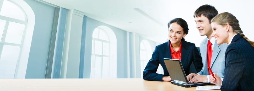 Photo of three office workers sitting at the table on the background of office building