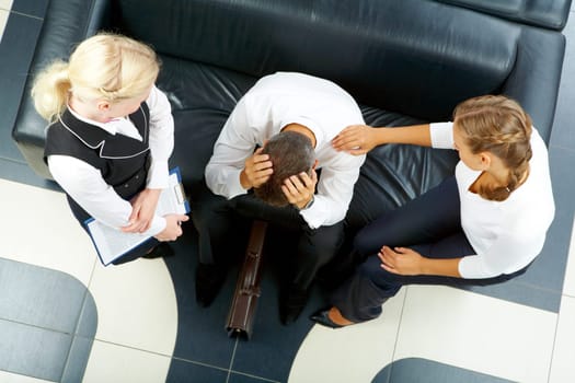 Two women reassuring troubled businessman touching head while sitting on sofa