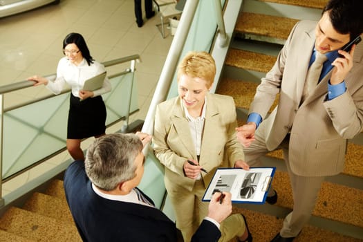 Photo of busy partners discussing papers while on stairs of office building