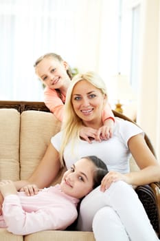 Portrait of happy woman and two daughters sitting on sofa and looking at camera