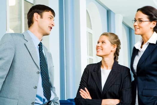 Photo of businessman and businesswoman speaking to each other in the office while the other woman standing near by and listening to them