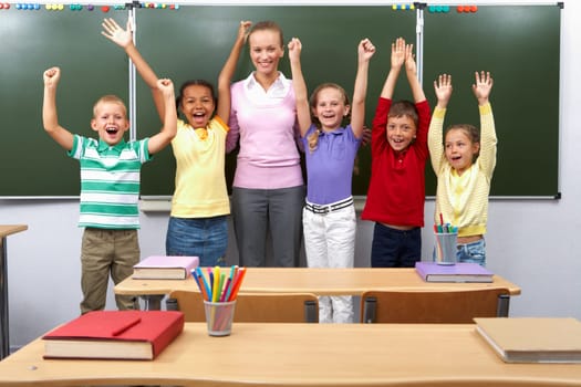 Line of cute schoolchildren raising arms with their teacher in the middle
