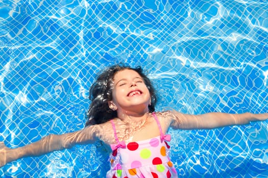 brunette children girl swimming in blue tiles pool floating closed eyes