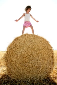 Girl playing over the round wheat dried bale outdoor summer