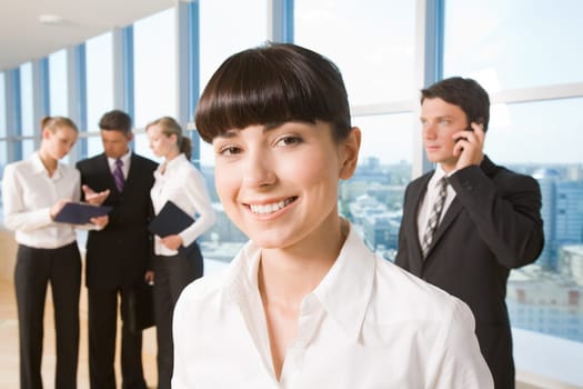 Portrait of happy businesswoman smiling at camera on background of working employees