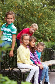 Portrait of happy friends resting on bench in park