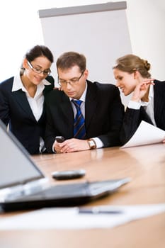 Three employees look at phone which the man holds at meeting