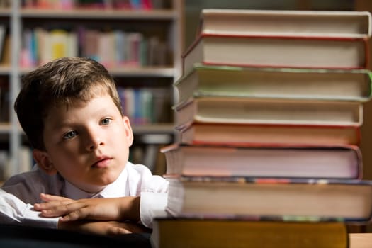 Face of diligent schoolboy looking at stack of books in the library