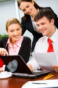 Vertical photo of a businessman looking at the screen of laptop with two businesswomen near by