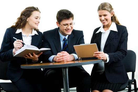 Photo of smiling young colleagues sitting next to each other at meeting and looking at the laptop screen together