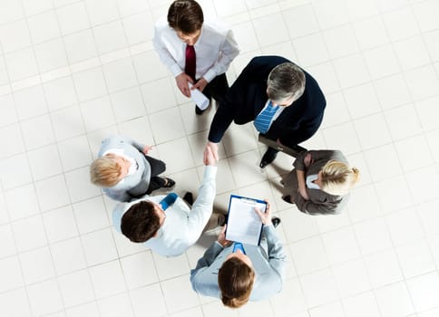 Photo of successful business partners handshaking after striking deal with some employees near by