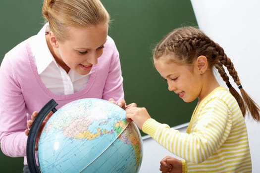 Portrait of cute girl and teacher looking at globe during lesson