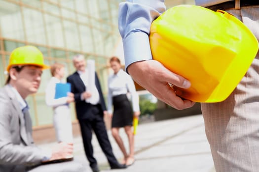 Close-up of builder holding helmet with working group at background