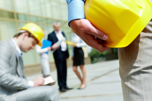 Close-up of builder holding helmet with construction at background