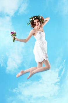Beautiful woman with bunch of flowers jumping against blue sky