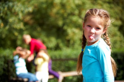 Portrait of funny girl looking at camera and showing tongue with her friends on background
